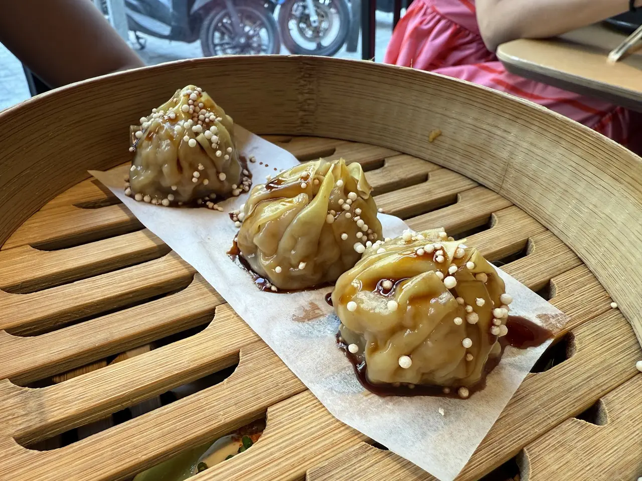 Steamed dumplings with glossy sauce and pearl garnish in a bamboo steamer
