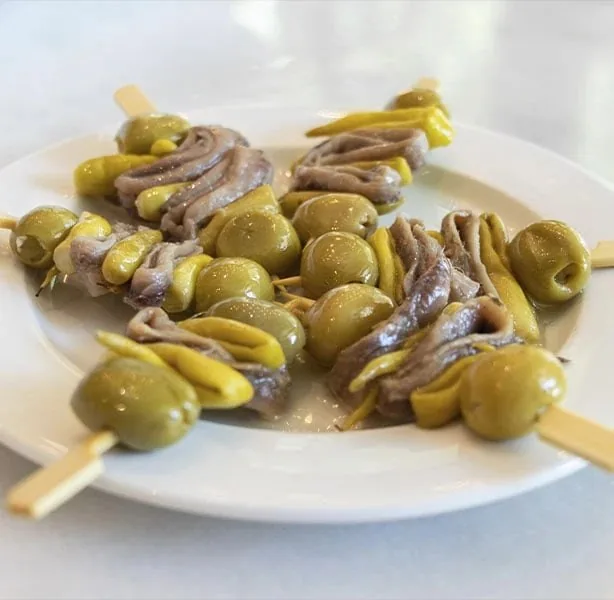 A white plate of gildas - skewers of green olive, pickled guindilla pepper and rolled anchovy - piled together