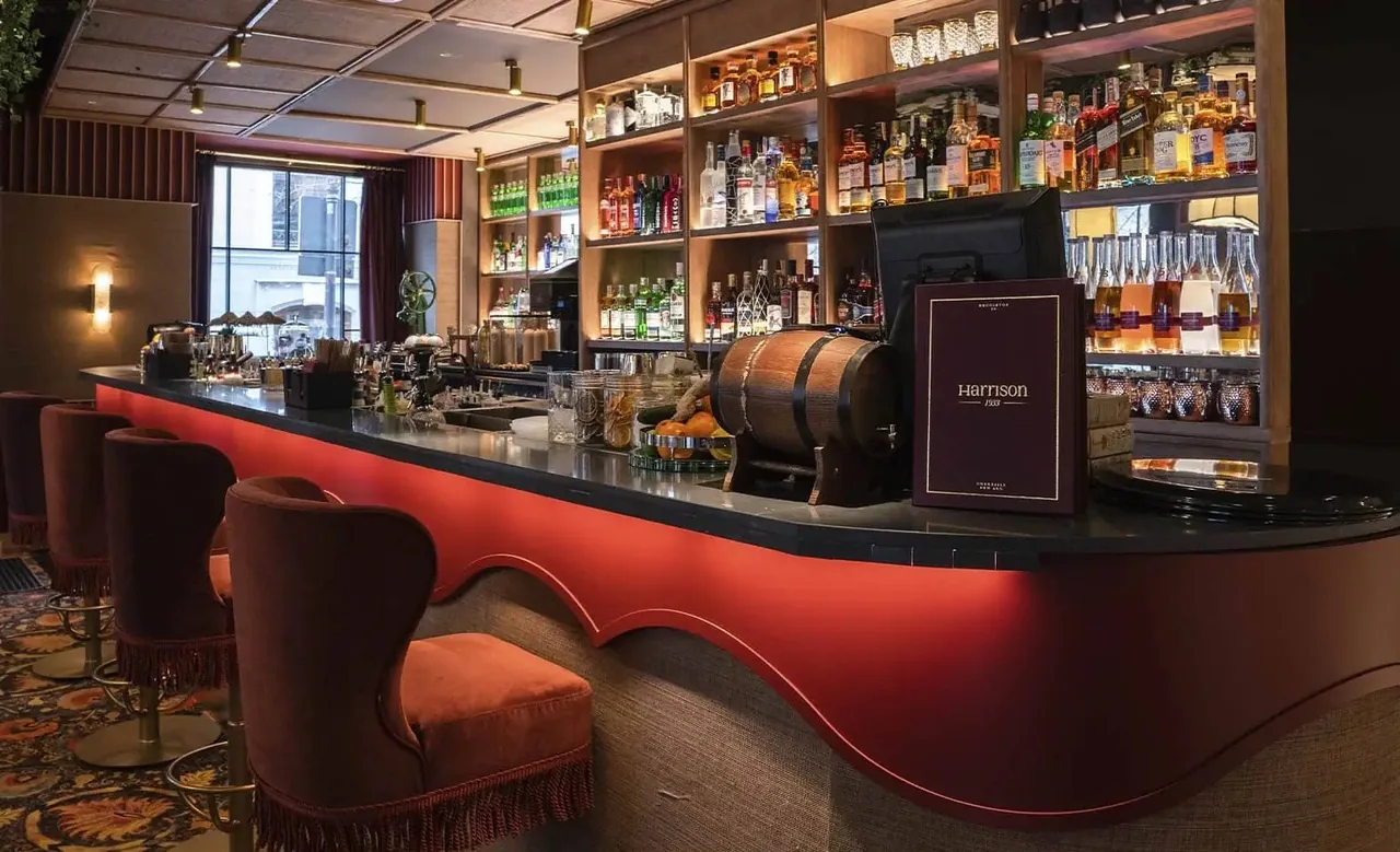 A bar counter with a red front and rows of bottles on shelves behind it