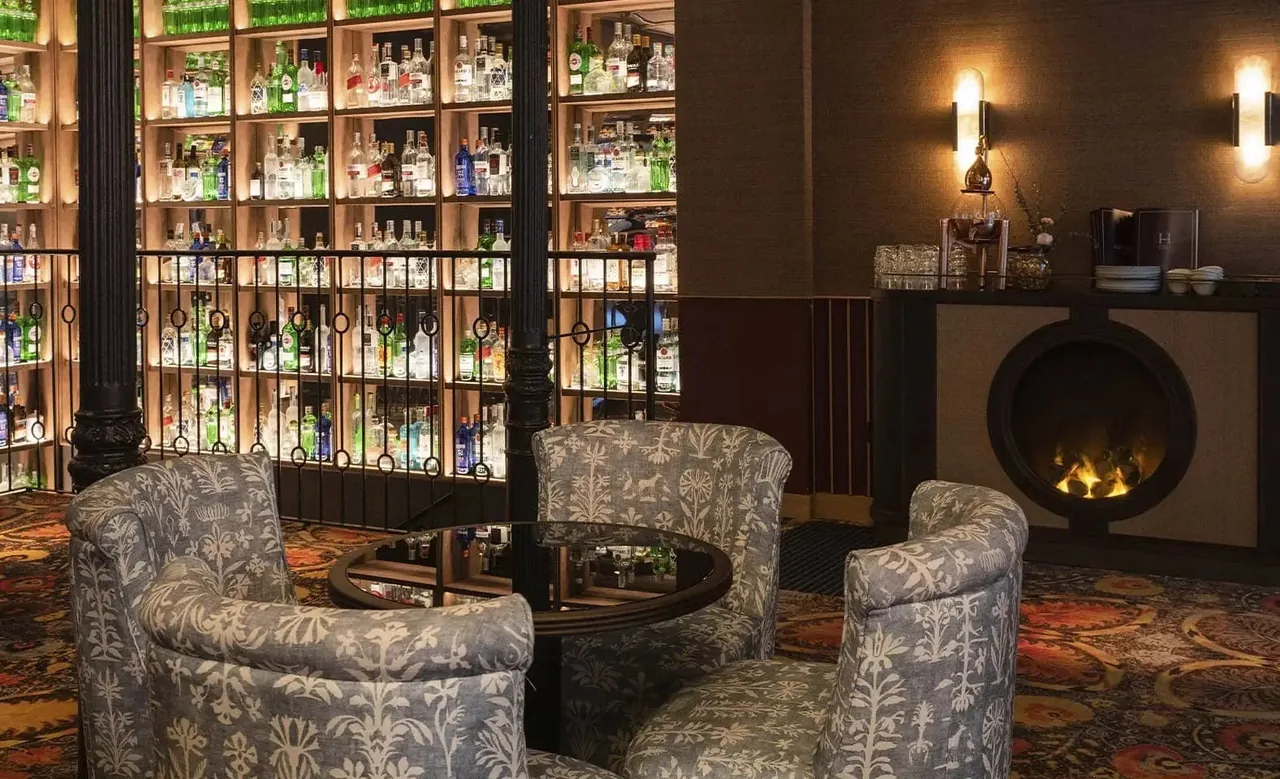 Armchairs and a fireplace in front of tall shelves of bottles