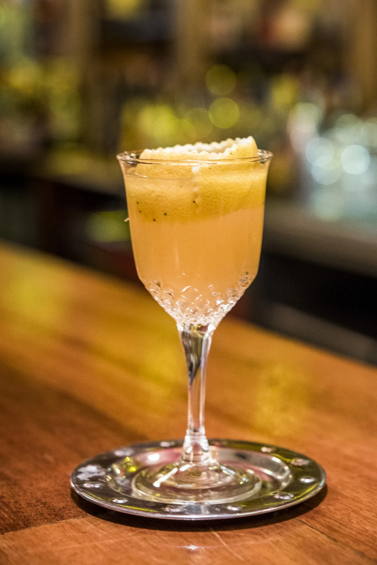 A pale yellow cocktail in a coupe glass on a wooden bar