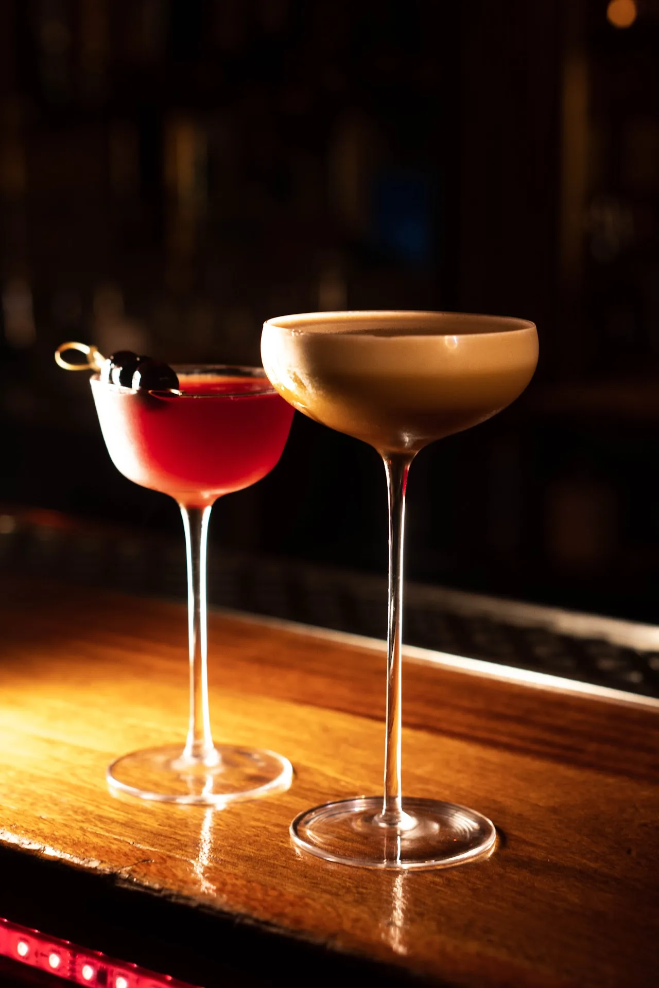 Two cocktails, one red and one tan-colored, on a bar counter