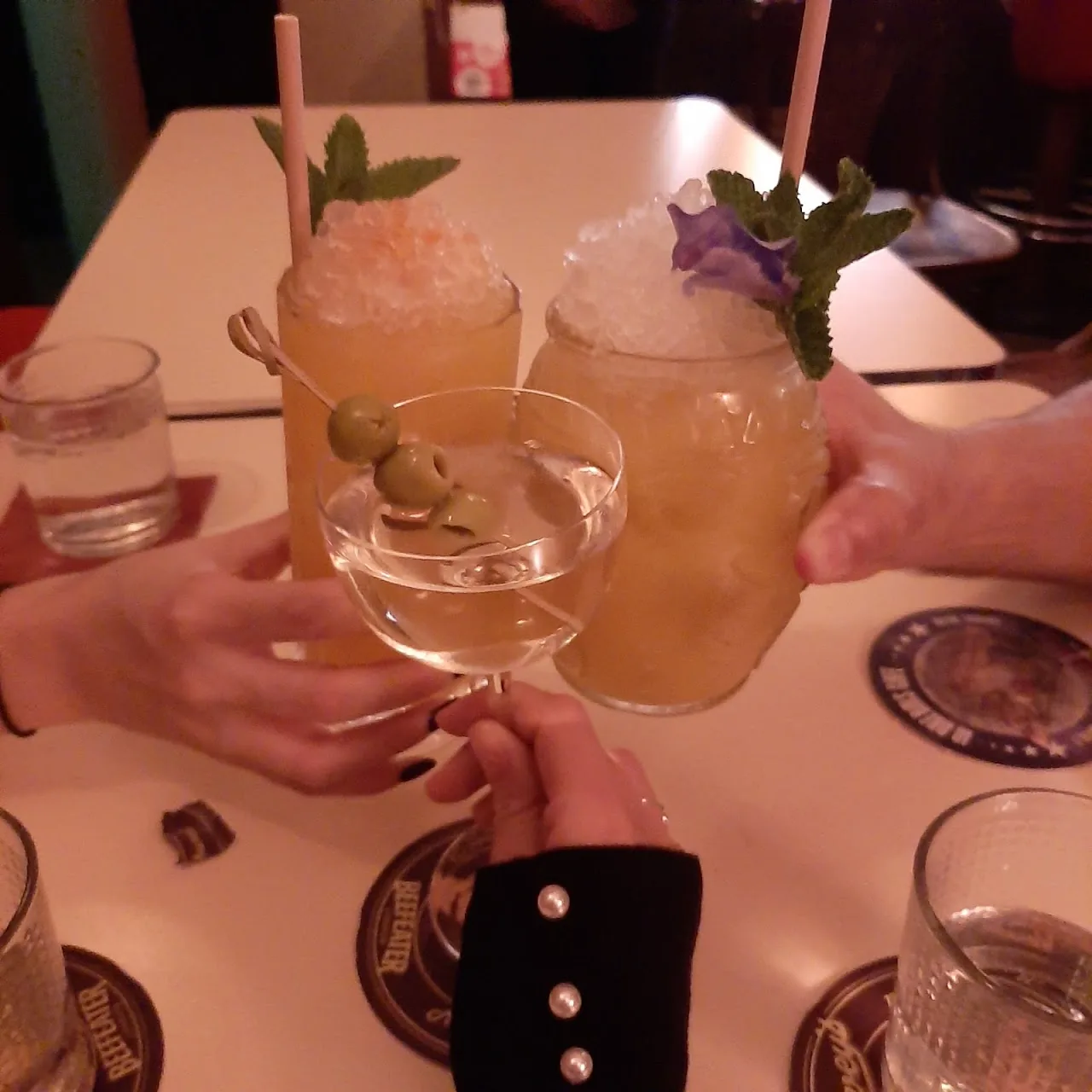 Two garnished cocktails held up at a table, one with mint