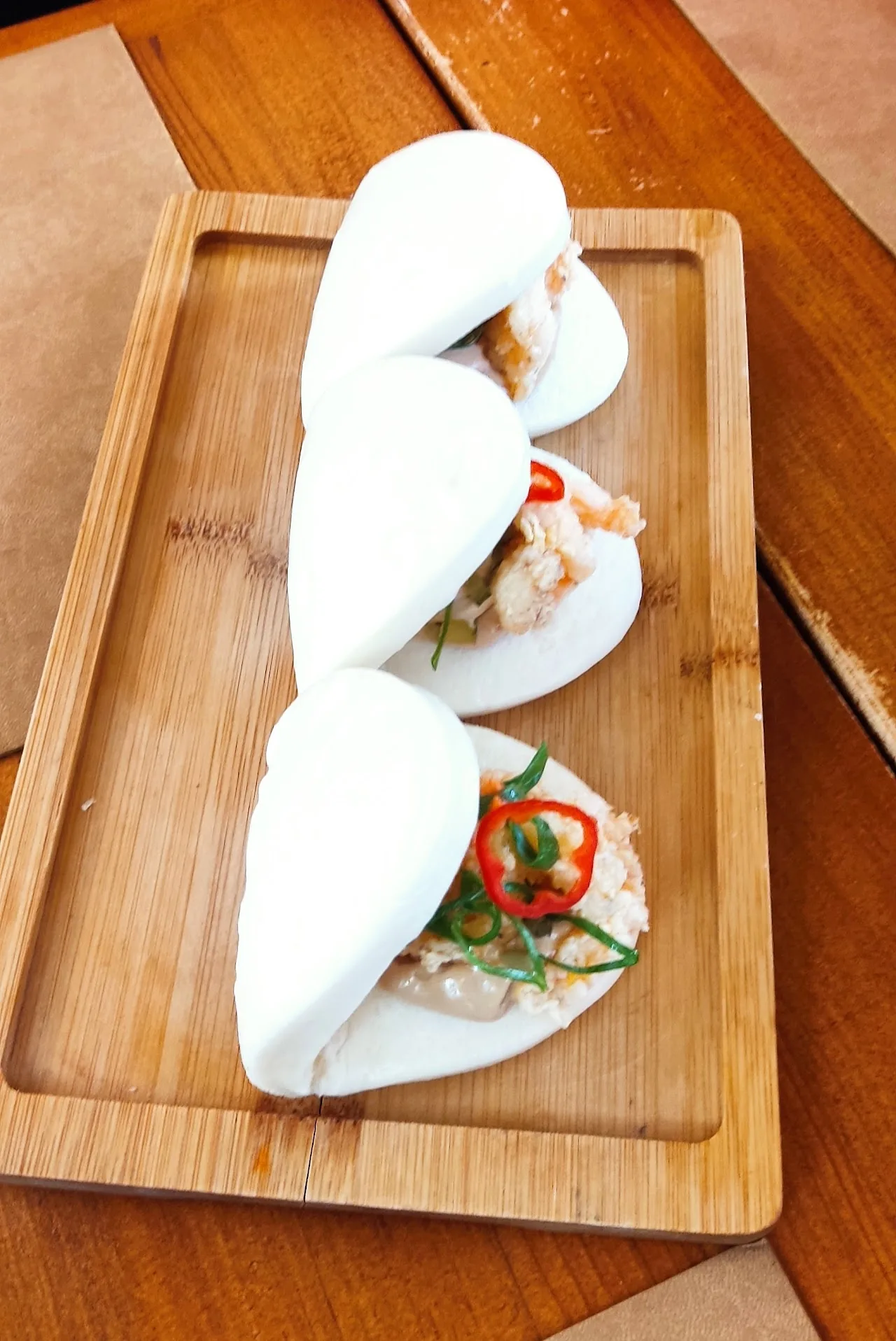 Three folded bao buns filled with meat and chili on a wooden board