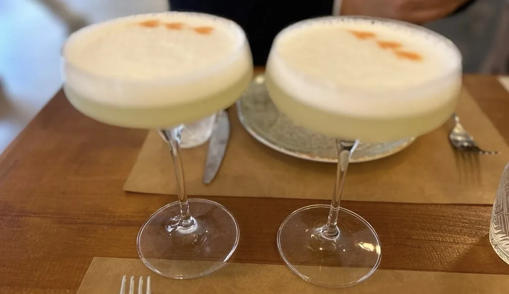 Two frothy pisco sour cocktails on a wooden tray