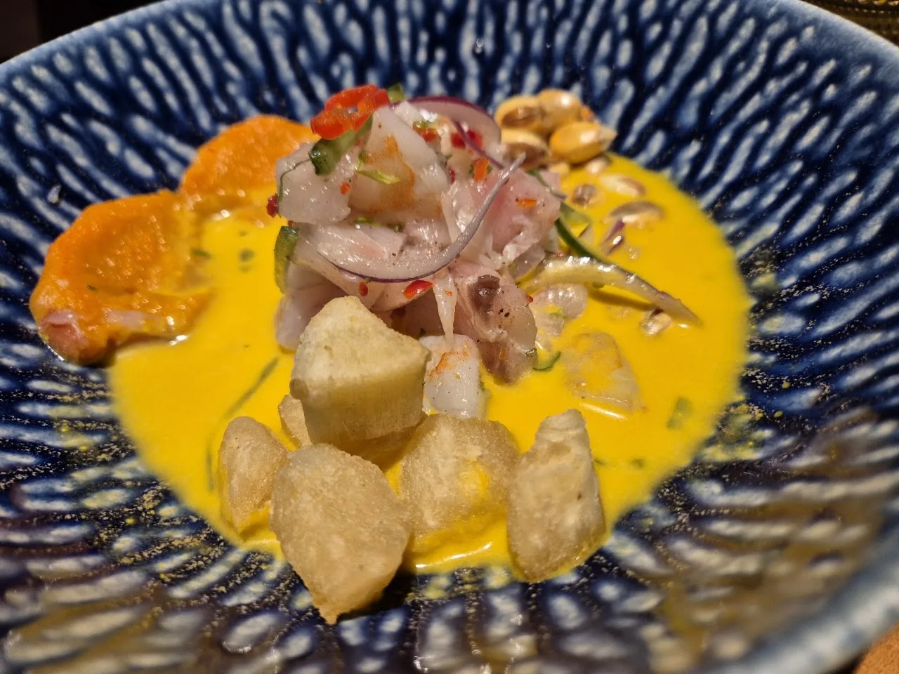 A ceviche dish with citrus sauce, sweet potato, and corn in a patterned bowl