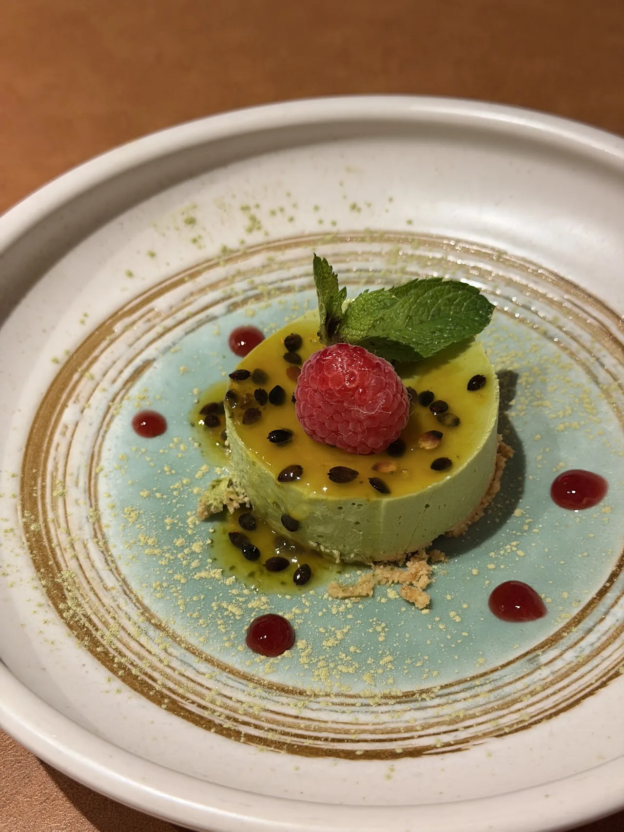 A green dessert with passion fruit sauce and a fresh raspberry