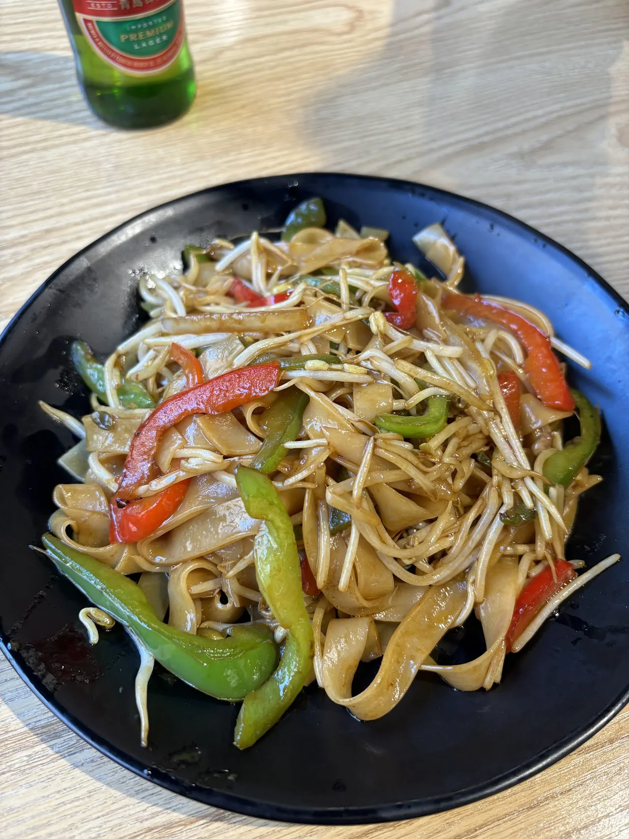 A black plate of noodles with green and red bell peppers