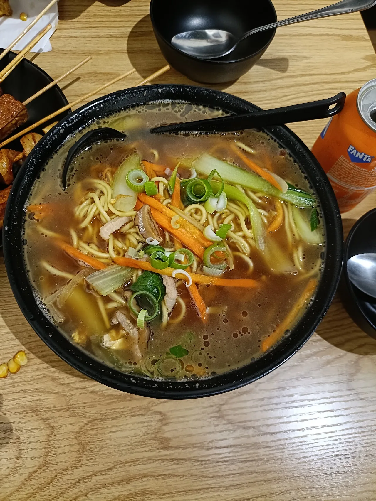 A bowl of noodle soup with carrots and scallions