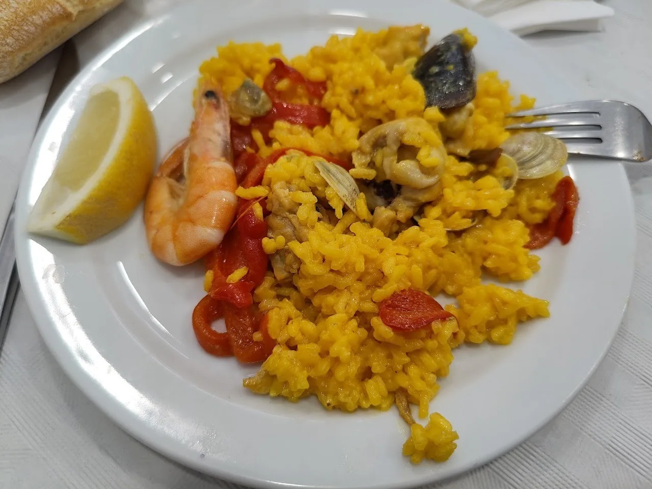 A white plate of yellow rice with prawns, mussels and peppers with a lemon wedge
