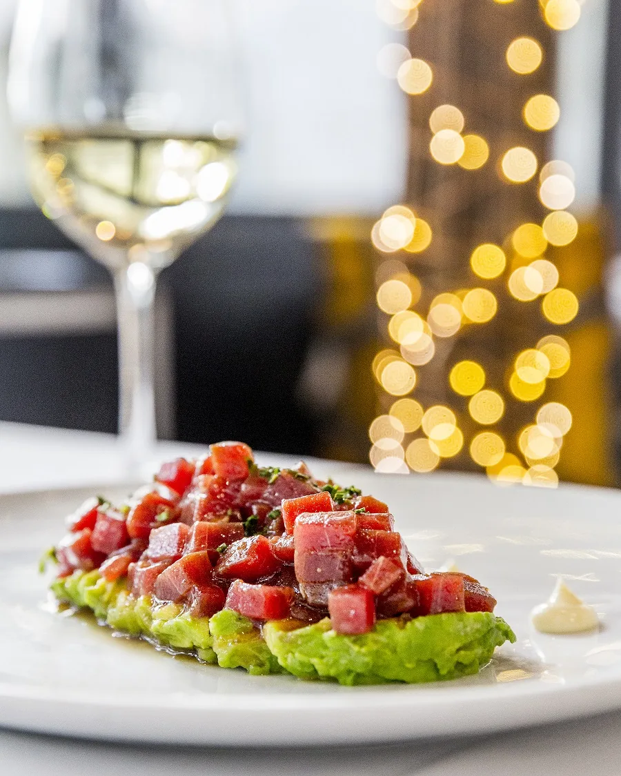 A tartare dish on a bed of lettuce with a glass of white wine