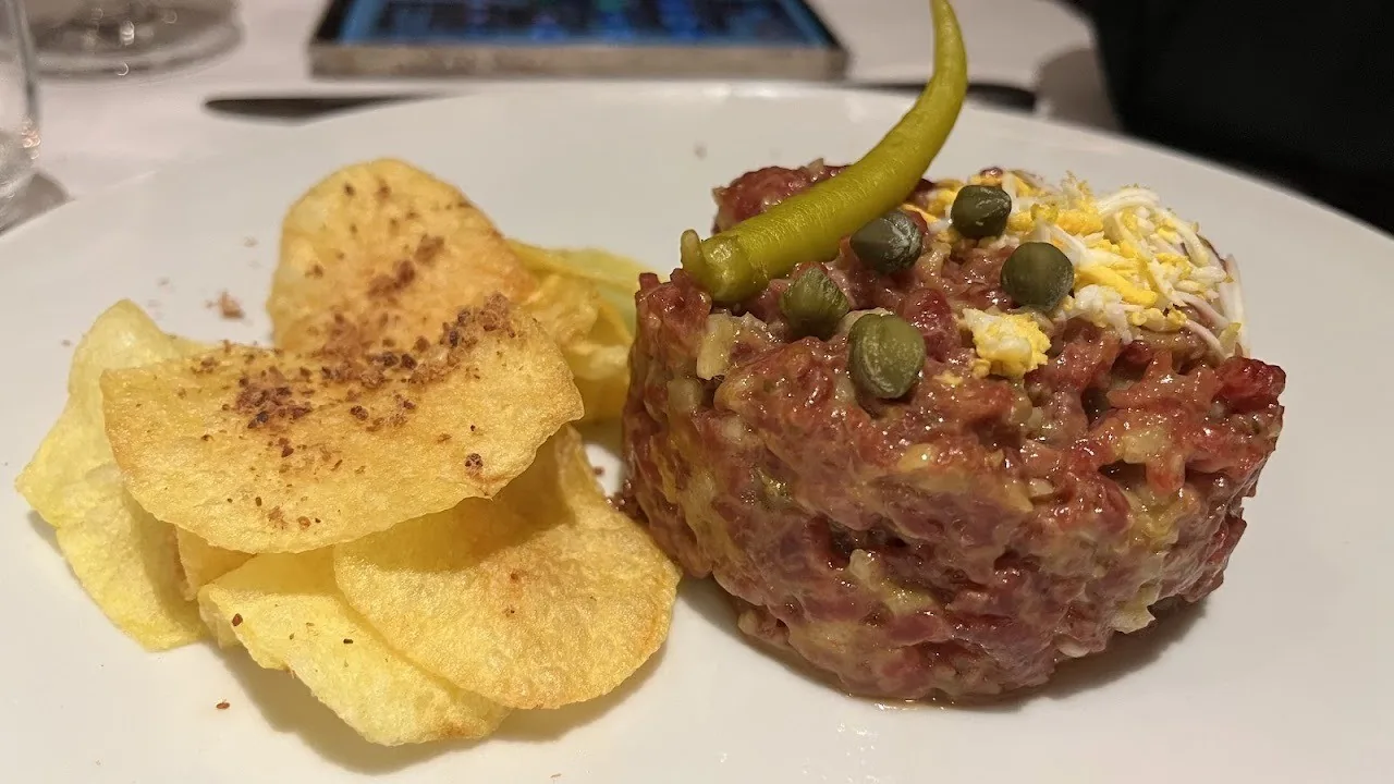 A mound of chopped raw beef with a green chilli and potato chips on a white plate