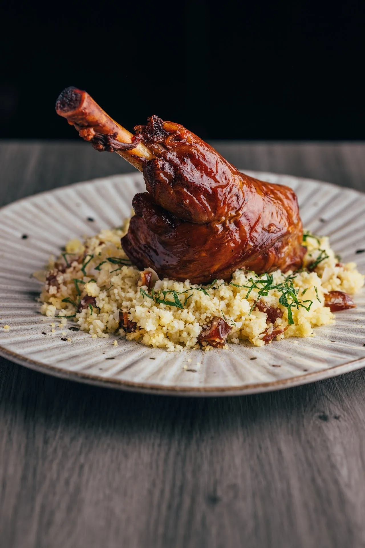 A roasted lamb shank on rice on a white plate
