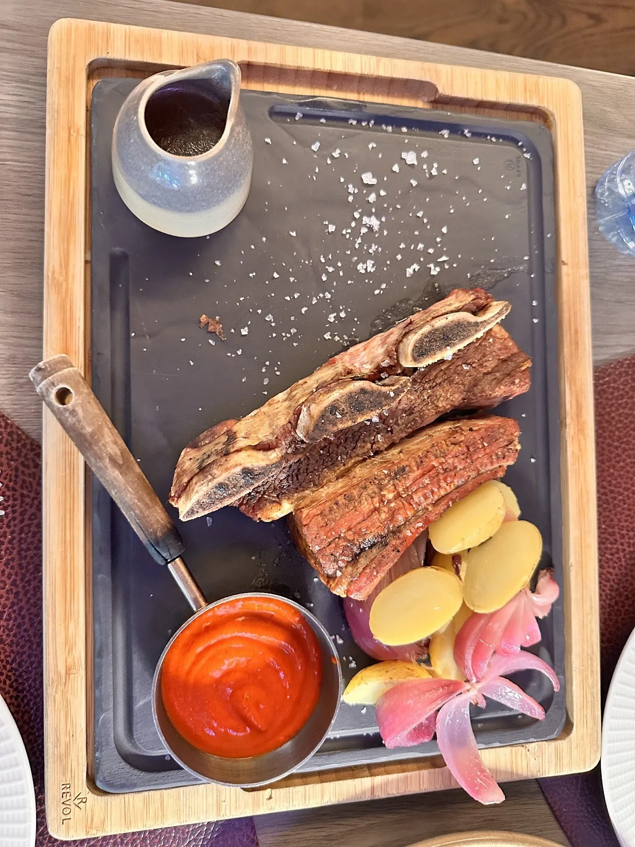 Grilled ribs and potatoes on a serving board with a red sauce