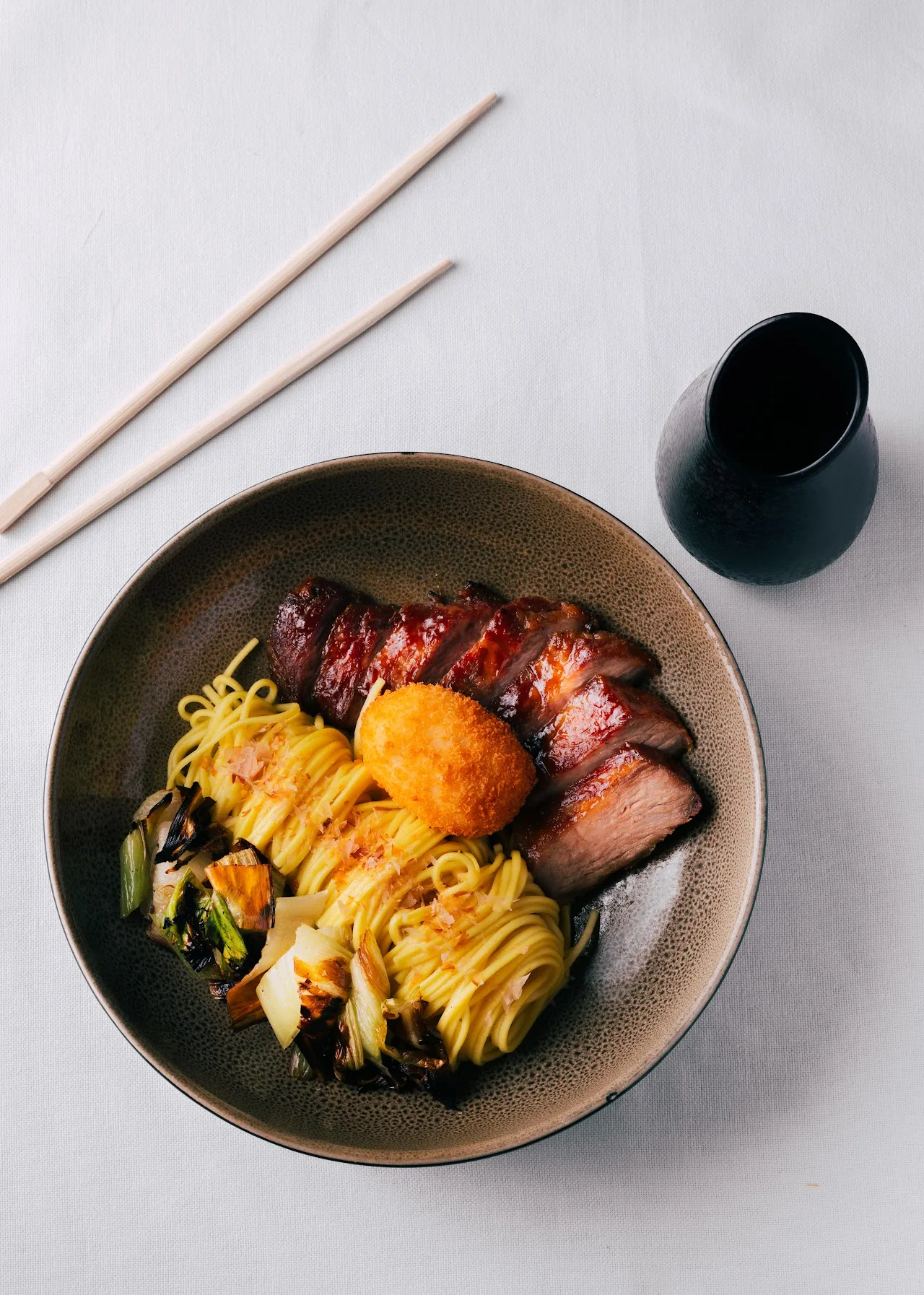 A bowl of noodles with pork belly and a soft egg