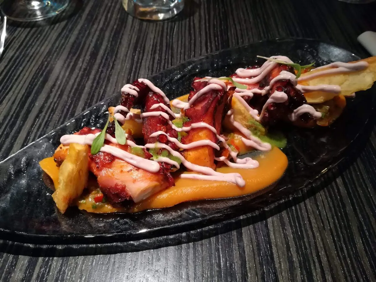 Grilled octopus with a sauce drizzle on a dark plate