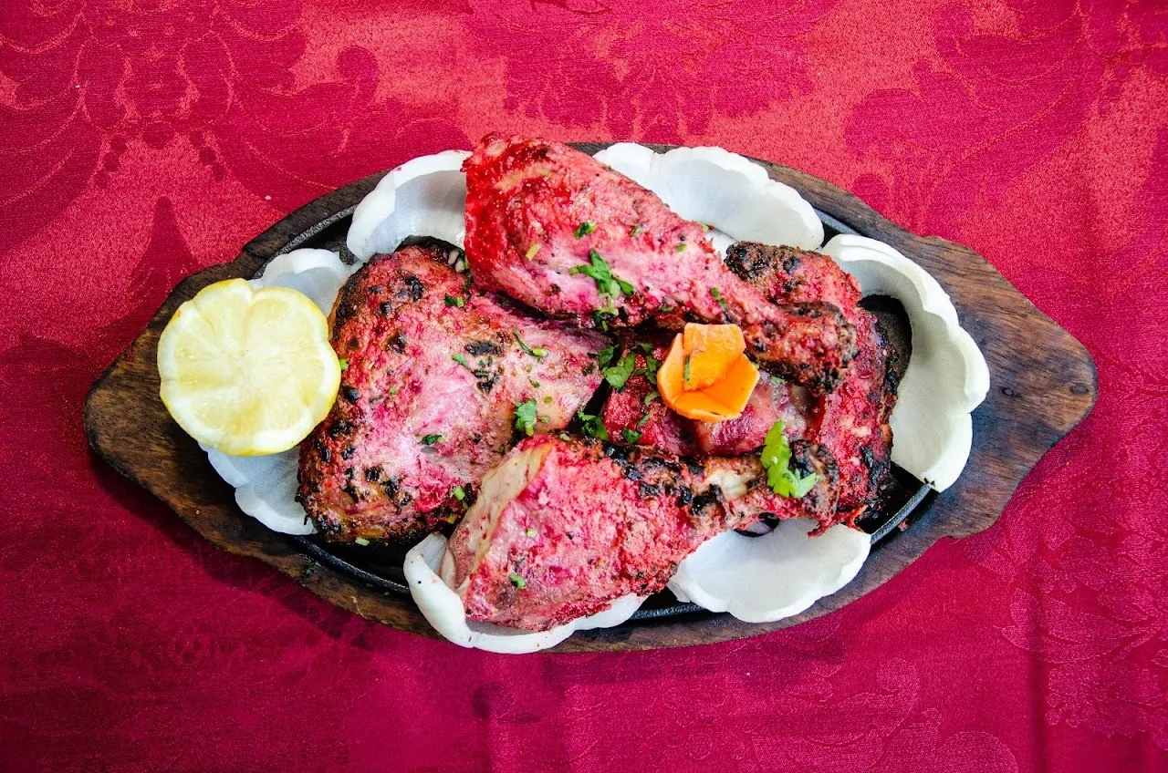 Red-marinated grilled chicken pieces with a lemon half on a wooden sizzling platter on a red tablecloth