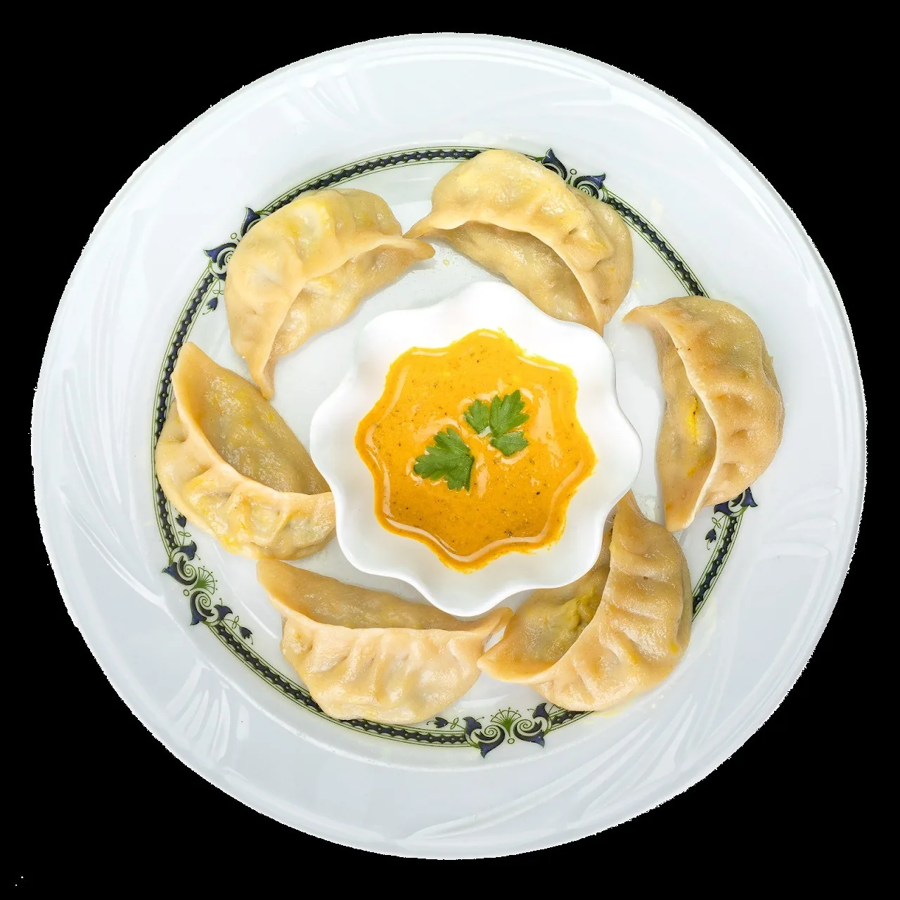 A white plate of pleated dumplings arranged around a small dish of orange sauce with parsley