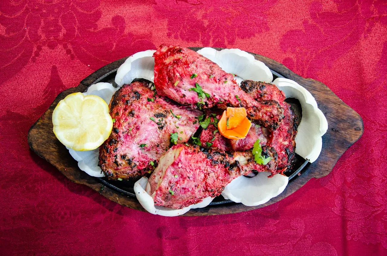 Tandoori chicken pieces on a sizzling platter with lemon