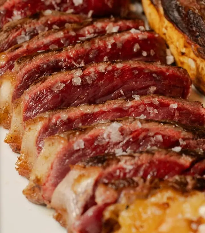 Slices of seared, rare cured beef scattered with flaky salt