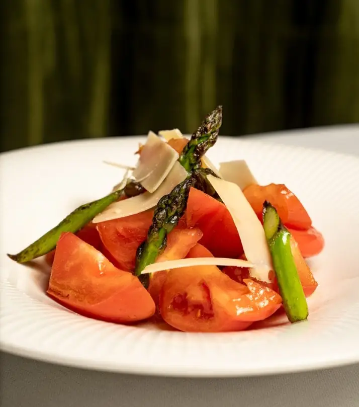 Tomato salad with green asparagus and shavings of aged cheese on a white plate