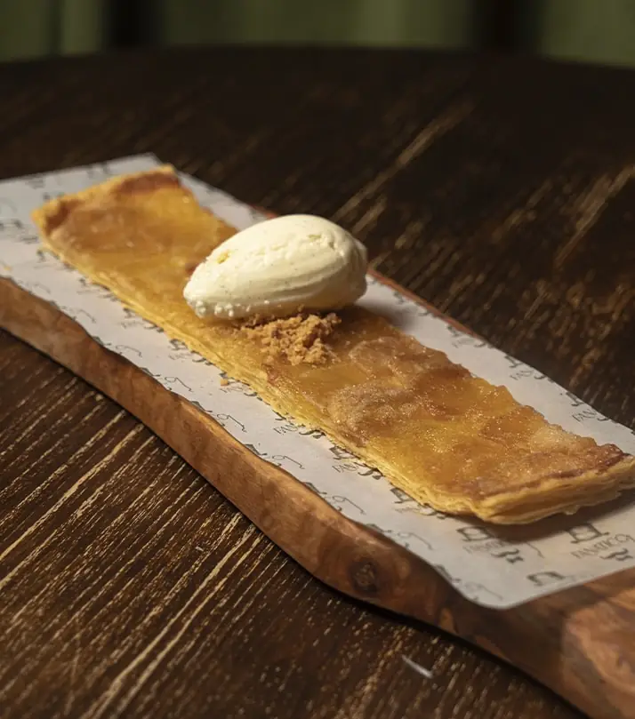A very thin apple tart with a scoop of ice cream on a wooden board