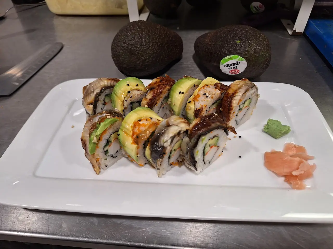 Sushi roll with eel and avocado topping, plated with wasabi and pickled ginger