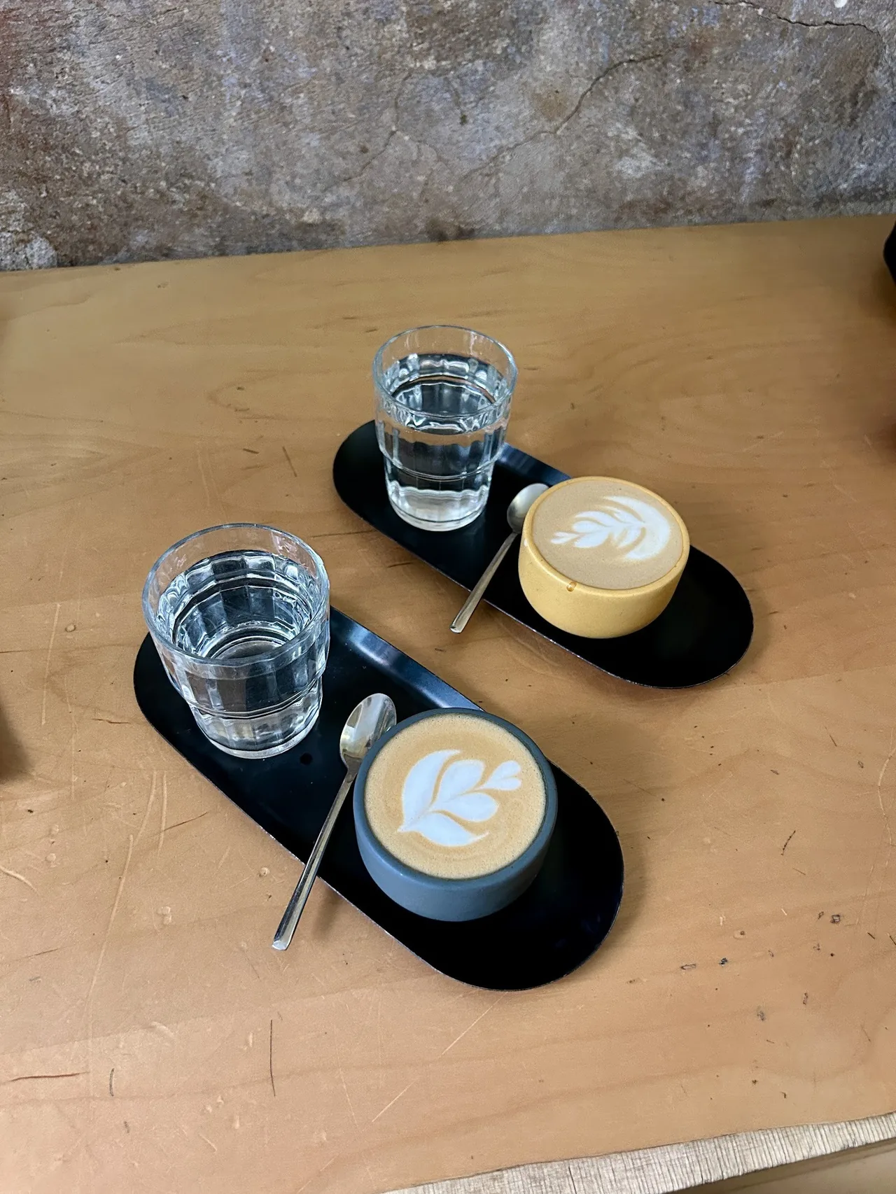 Two small flat white coffees with latte art and glasses of water on a black tray, seen from above