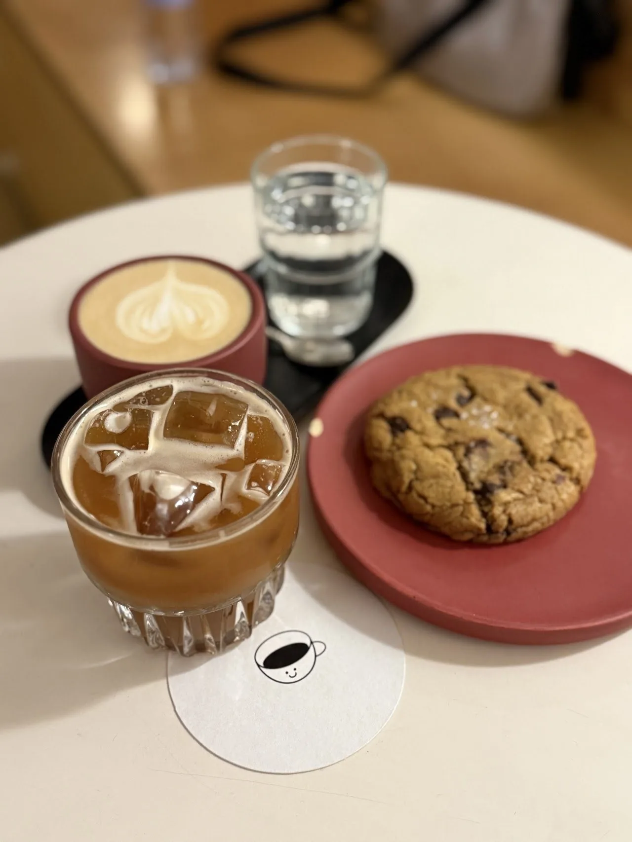 An iced coffee, a latte with art and a chocolate chip cookie on a small round table