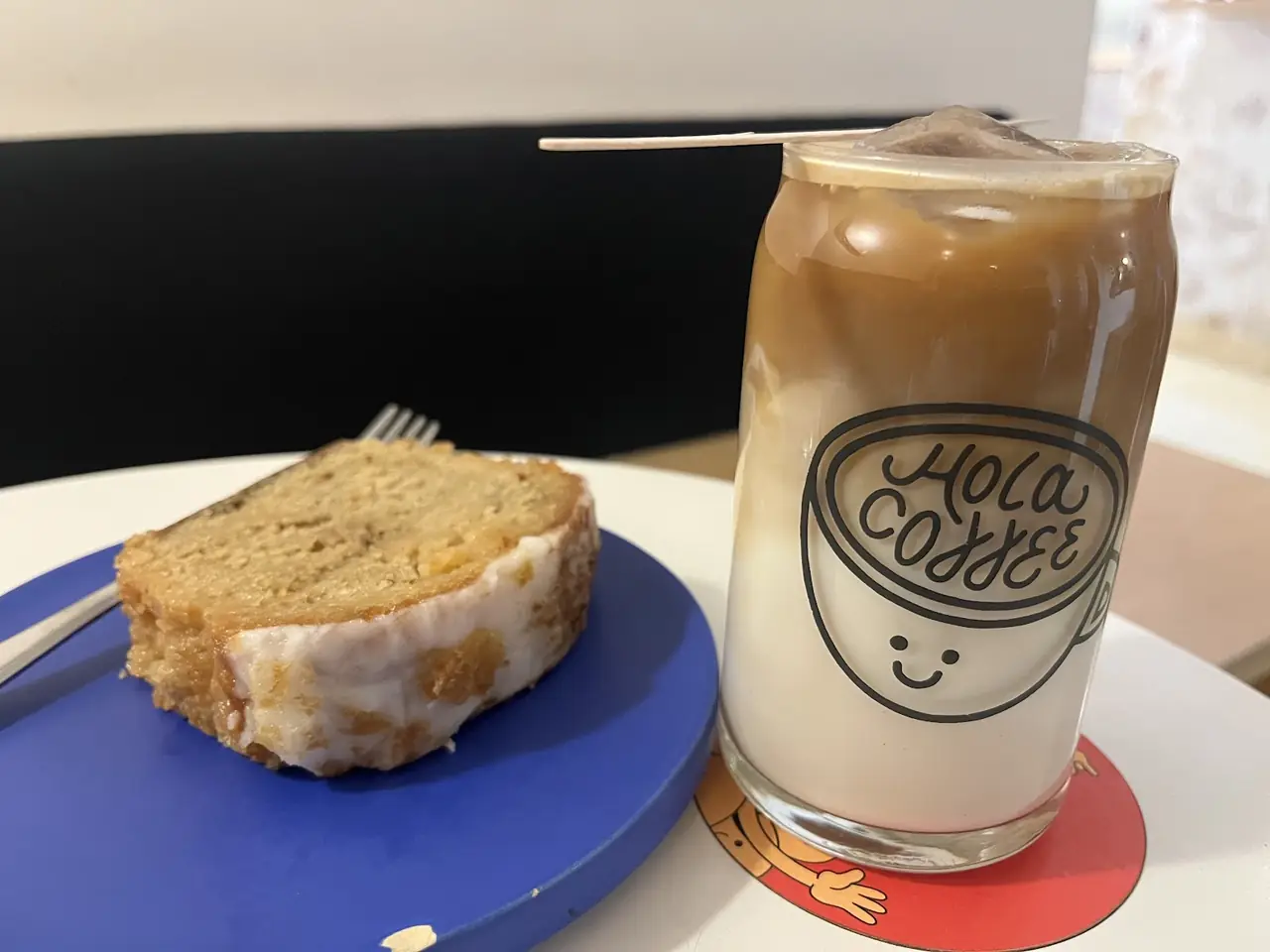 Iced latte in a branded glass beside a glazed pound cake slice on a blue plate