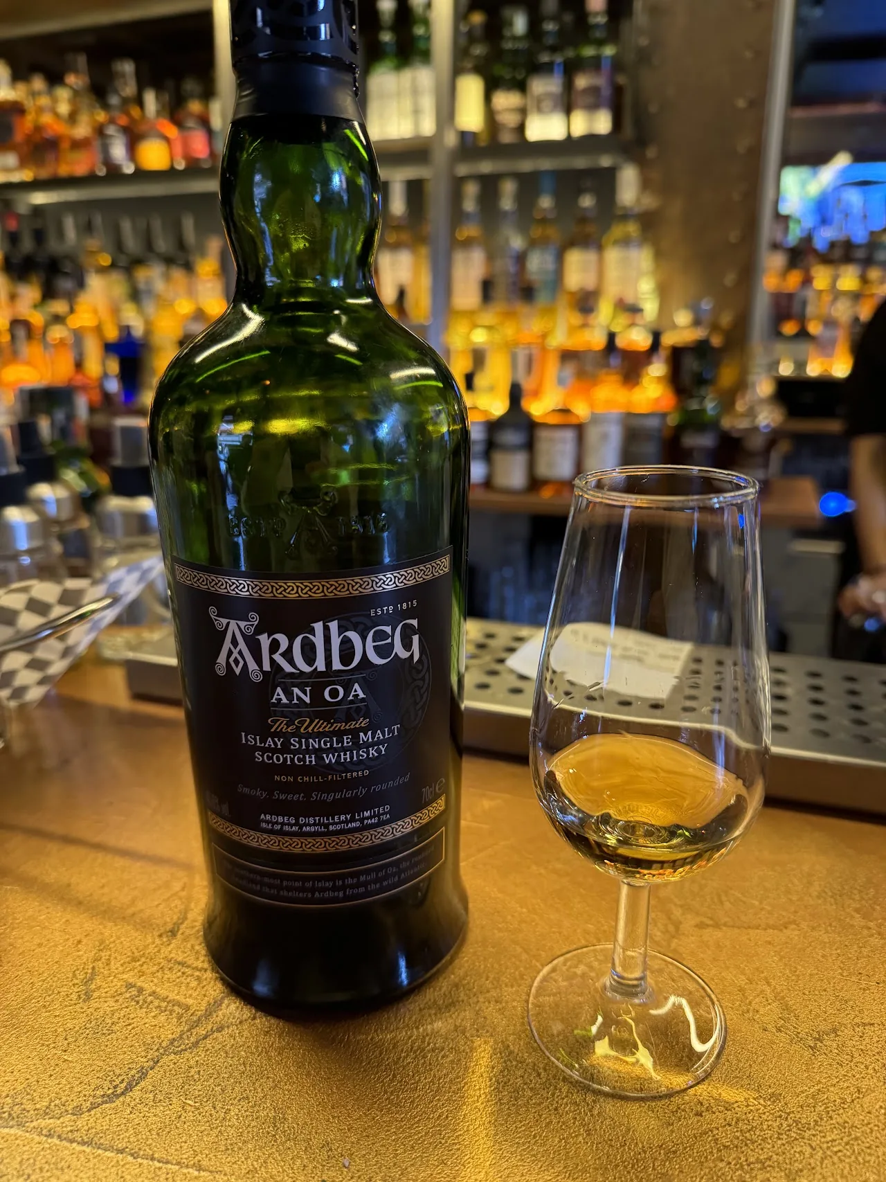A glass of amber whisky beside its bottle on a bar counter