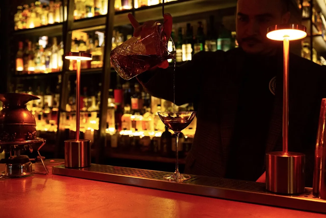 A bartender pouring a shaken cocktail into a coupe glass