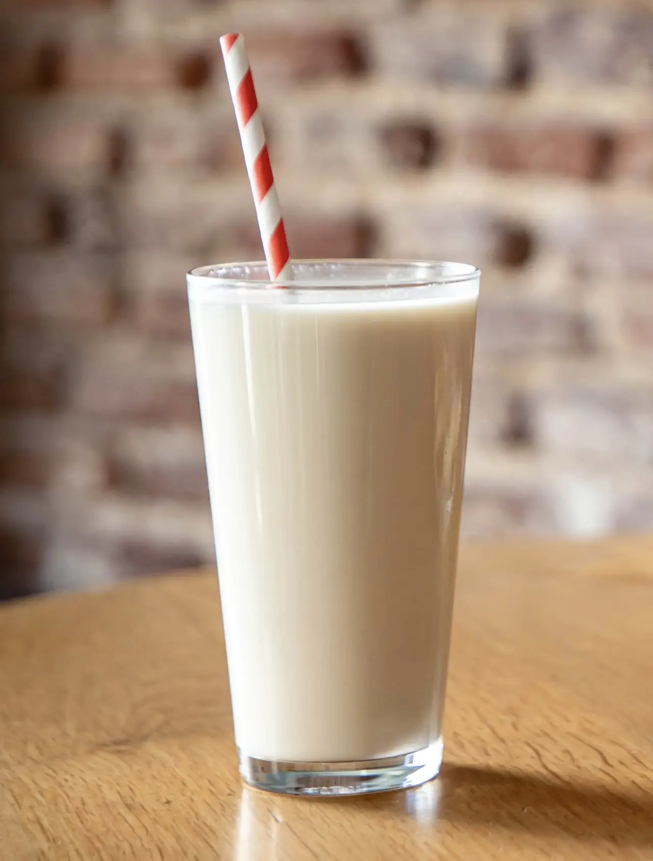 Glass of horchata with a red-and-white striped straw on a wooden table