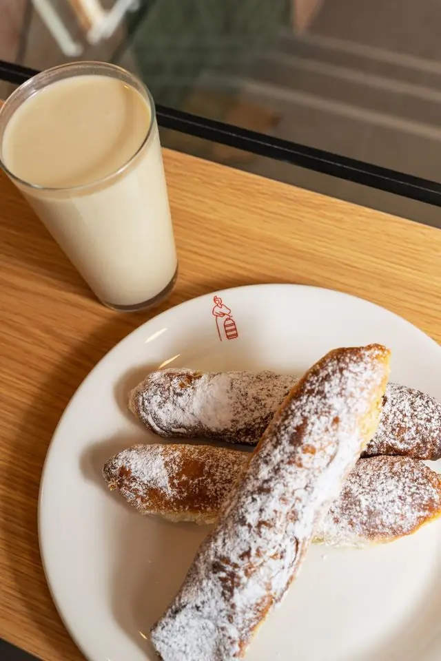 Glass of horchata beside a plate of sugar-dusted fartones pastries