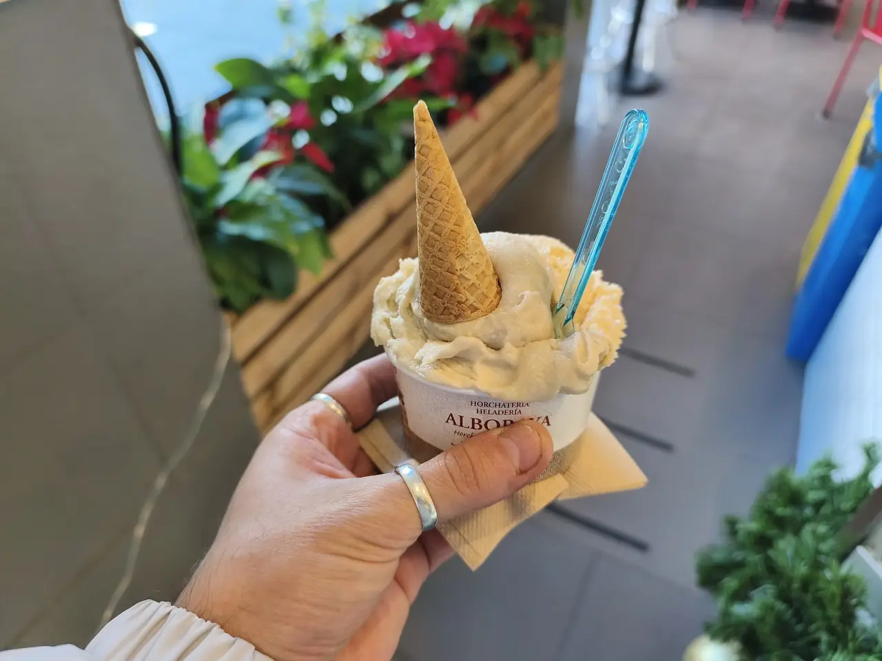 Hand holding a cup of horchata gelato topped with a mini cone, in an Alboraya-branded cup