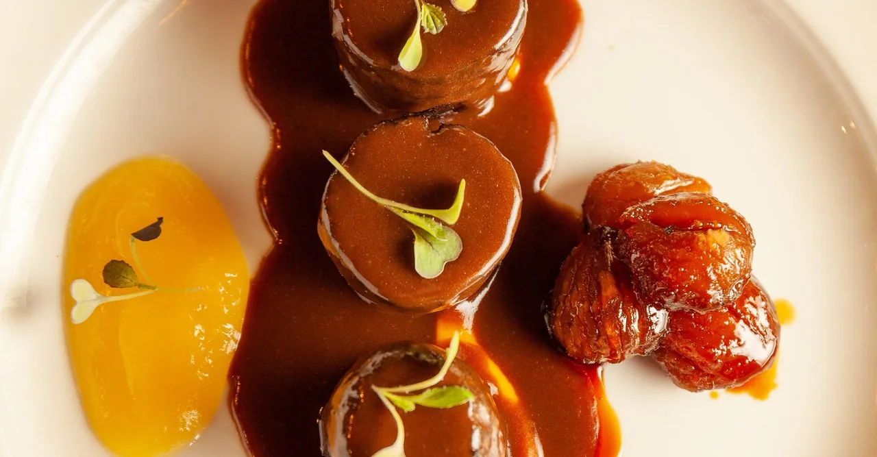 Round medallions of meat in a glossy brown sauce with an orange puree on a white plate