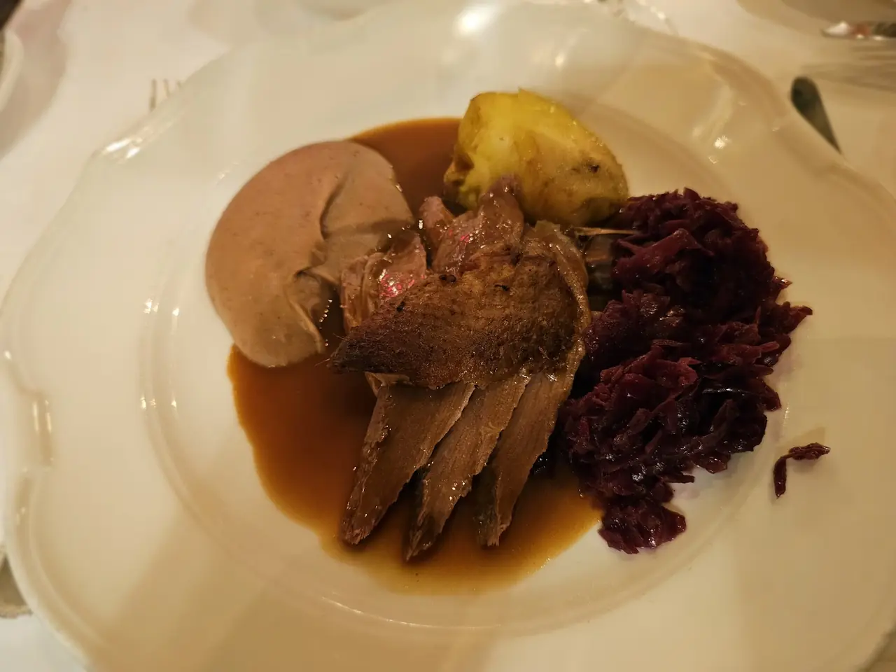 Sliced roasted meat in gravy with red cabbage and a chestnut puree quenelle on a white plate