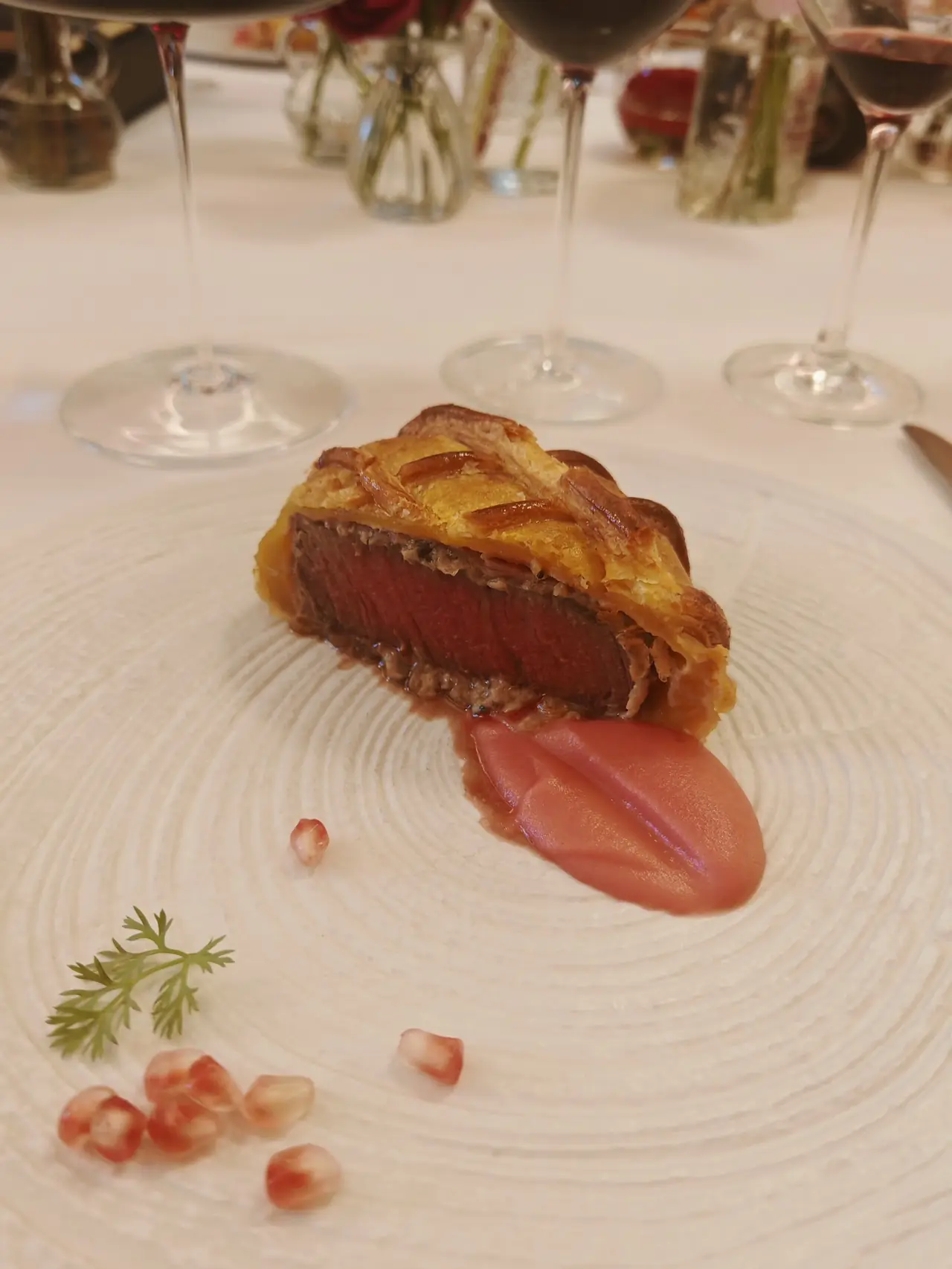 Sliced beef Wellington showing pink interior, plated with sauce and pomegranate seeds
