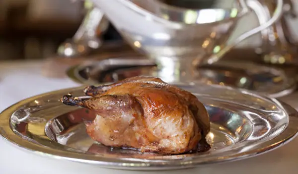 Whole roasted small game bird on a silver plate with a sauce boat behind