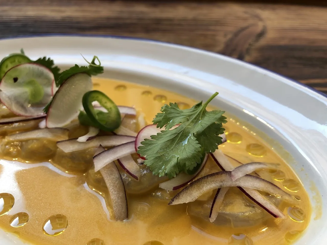 A shallow bowl of a yellow broth with sliced radish, herbs and green chili