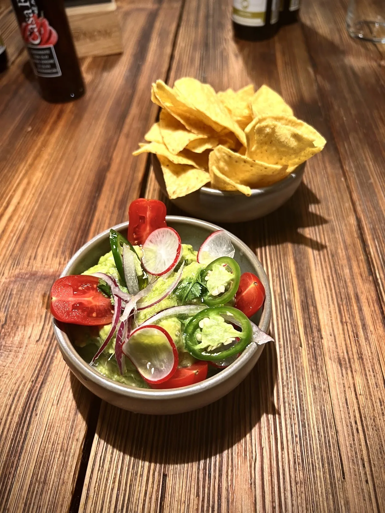 A bowl of fresh salad beside a bowl of tortilla chips on a wooden table