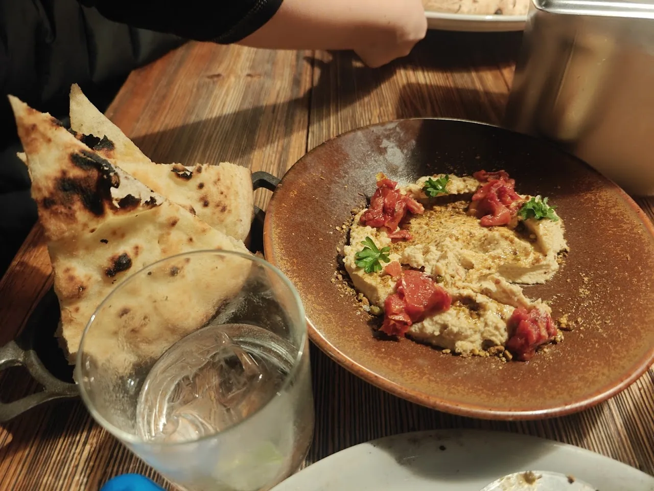 Grilled flatbread beside a bowl of hummus topped with cured meat