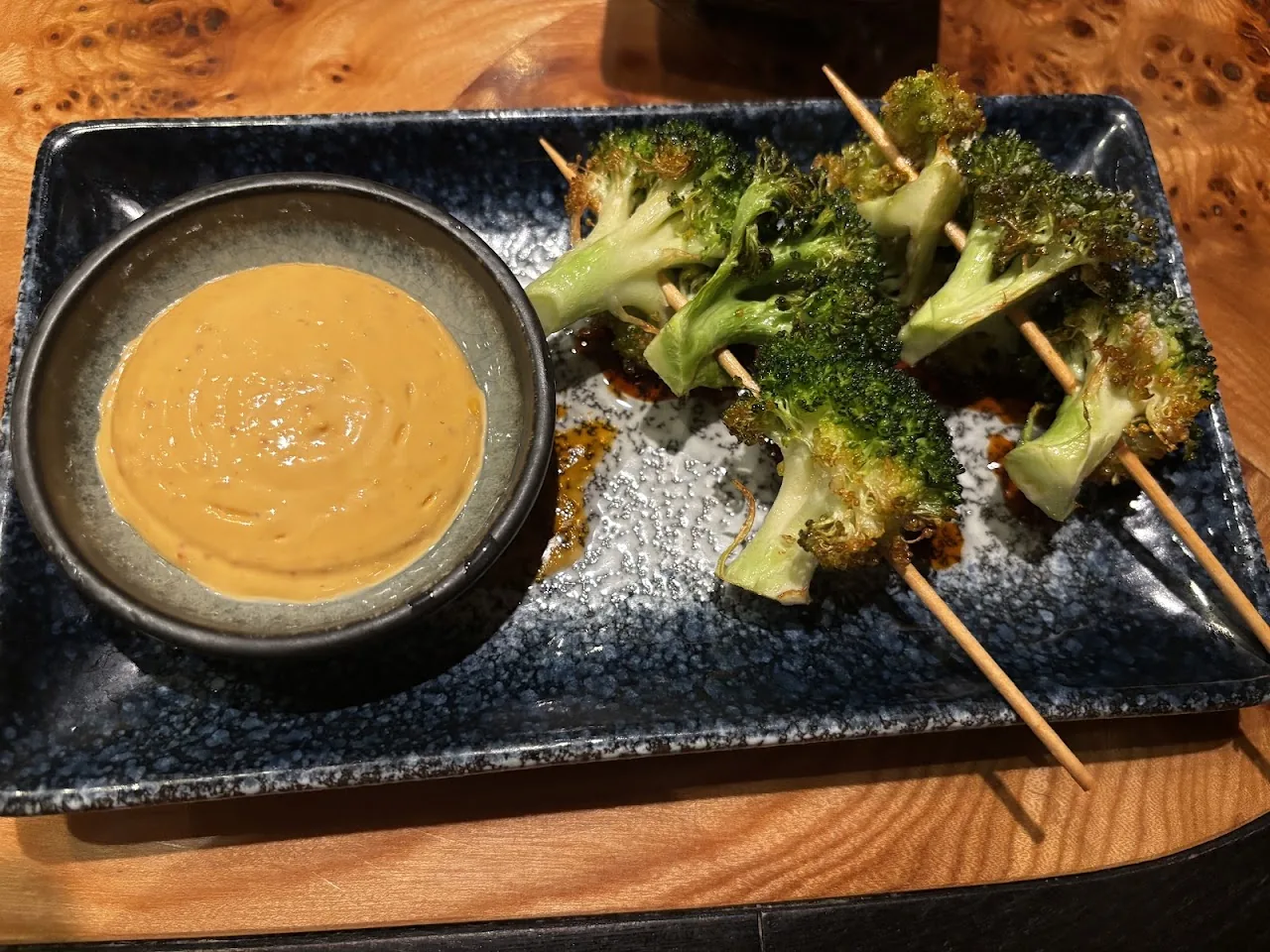 Broccoli skewers beside a bowl of orange dipping sauce