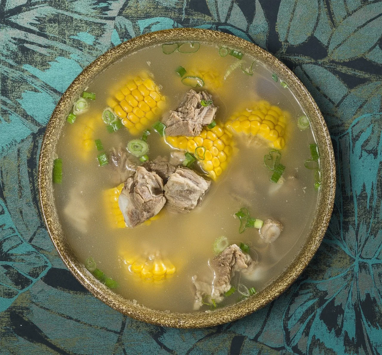 A bowl of soup with pork and corn on the cob
