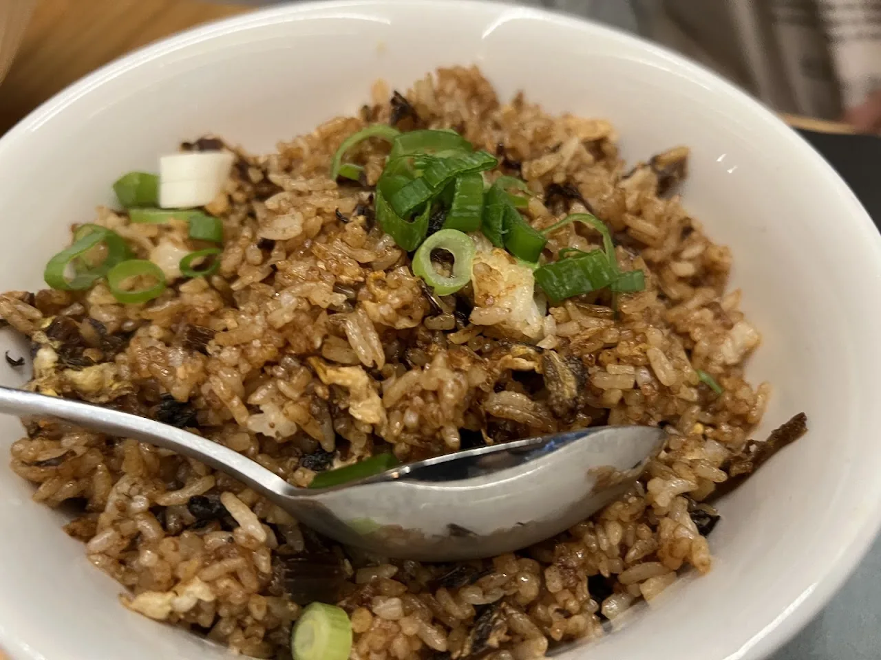 A bowl of fried rice with scallions and a spoon