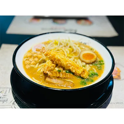 Bowl of ramen in a black lacquer bowl with a tempura prawn, a halved marinated egg, bean sprouts, chashu and spring onion
