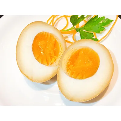 Two halves of a soy-marinated egg on a white plate with shredded carrot and a parsley sprig