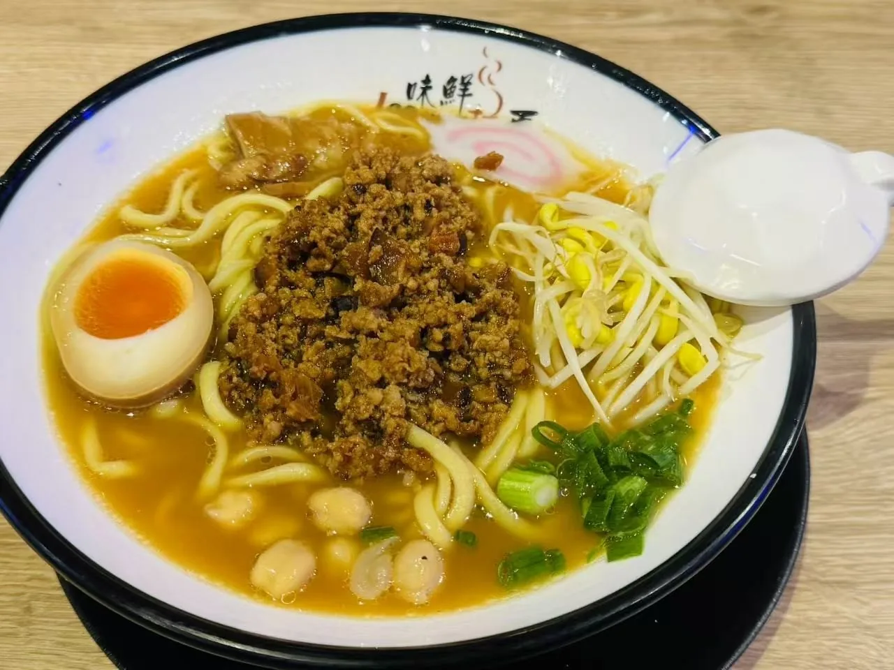 A bowl of noodles in golden broth topped with minced meat, a halved egg and bean sprouts