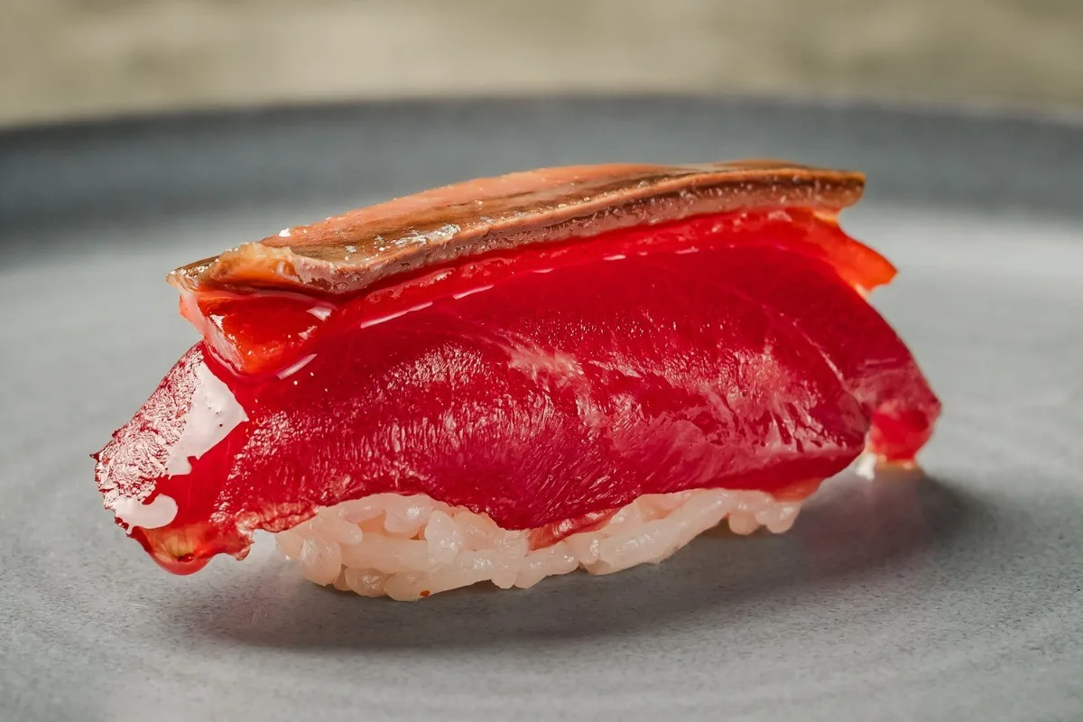 A piece of tuna nigiri with a thin strip on top on a grey plate