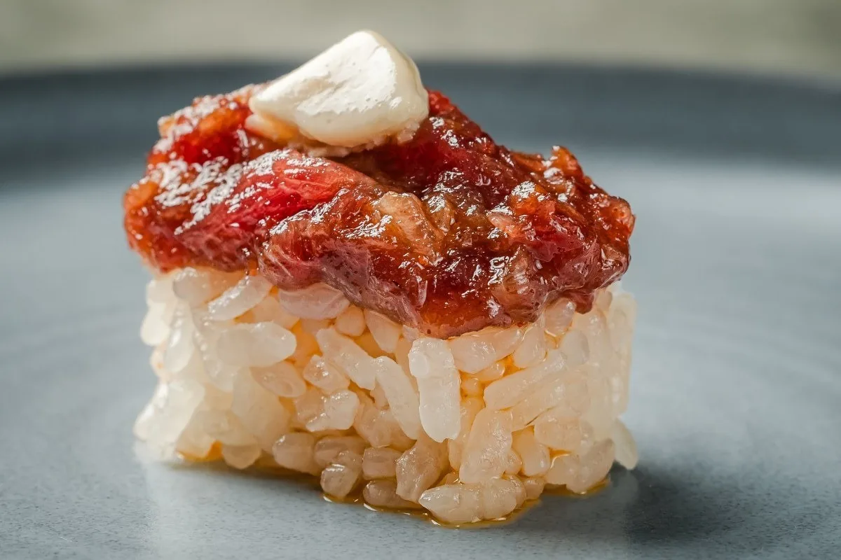 A piece of nigiri topped with red tuna and a white cream on a grey plate